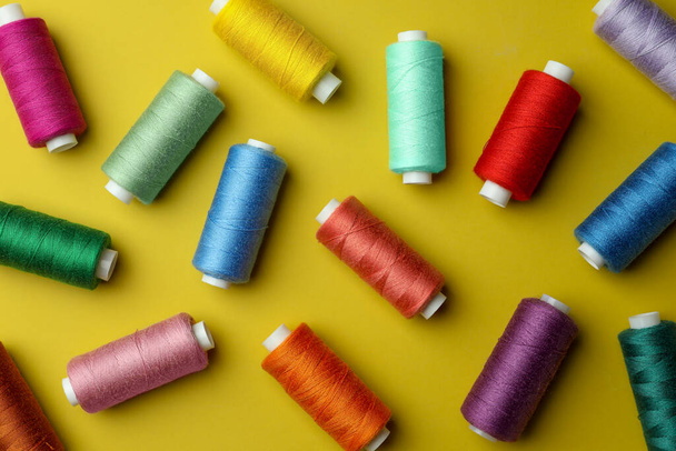 Different colorful sewing threads on yellow background, flat lay - Photo, image