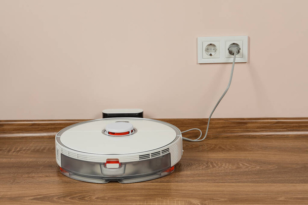 Robotic vacuum cleaner charging on wooden floor indoors - Zdjęcie, obraz