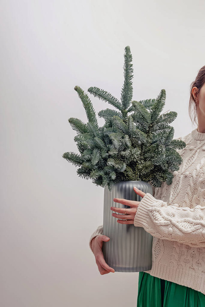 Unrecognizable woman holding a glass vase with decorative Christmas tree branches - Foto, afbeelding
