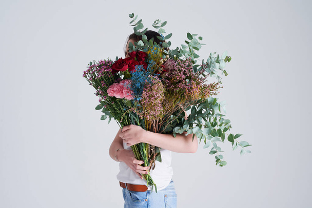 Pensi che sia un fiore selvatico? Studio foto di una donna irriconoscibile che si copre il viso con fiori su uno sfondo grigio - Foto, immagini