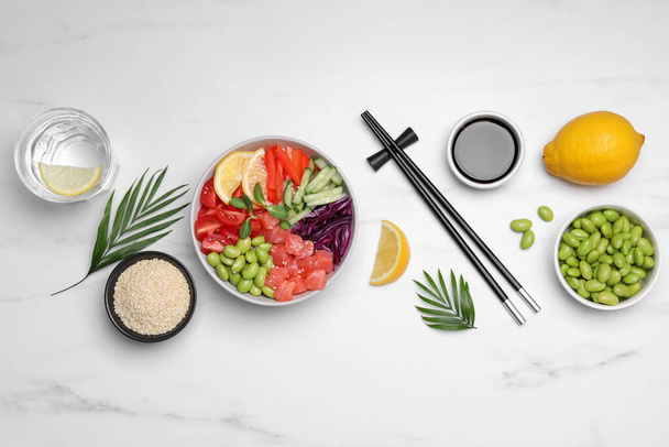 Poke bowl with salmon, edamame beans and vegetables on white marble table, flat lay - Fotó, kép