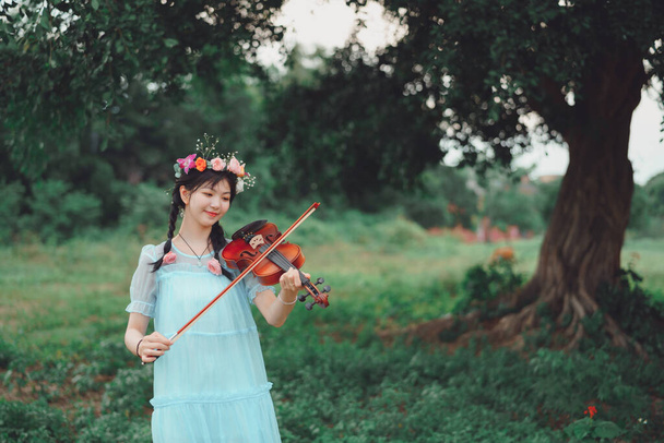 The girl is playing the violin under the big tree - 写真・画像