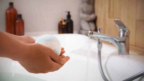 Woman holding bath bomb above tub indoors, closeup. Space for text - Foto, Imagen