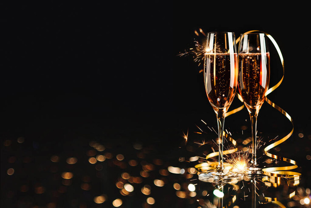 Zwei Gläser mit rosa Champagner, goldener Serpentine und Bokeh auf schwarzem Hintergrund - Foto, Bild