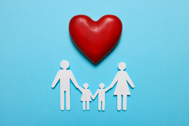 Paper family figures and red wooden heart on light blue background, flat lay. Insurance concept - Foto, imagen