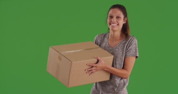 Iloinen valkoinen tyttö kuljettaa suuri tyhjä laatikko ja seisoo vihreällä näytöllä. Onnellinen nuori nainen, jolla on valolaatikko vihreän ruudun seinän edessä. 4 k. - Materiaali, video