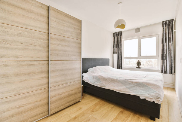 Kényelmes ágy díszítő takaróval elhelyezett üveg ajtó és szekrény tükörrel a világos hálószobában - Fotó, kép