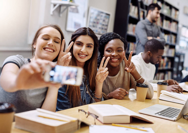 Hodně štěstí všem začínajícím zkouškám. skupina mladých žen, které se společně věnují selfie při studiu v univerzitní knihovně - Fotografie, Obrázek