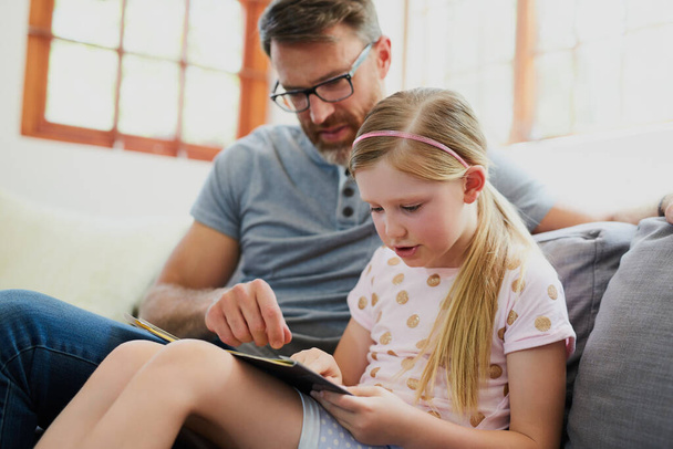 Lire ensemble l'aide à mieux lire. un père mûr et sa fille adorable lisant un livre ensemble sur le canapé à la maison - Photo, image