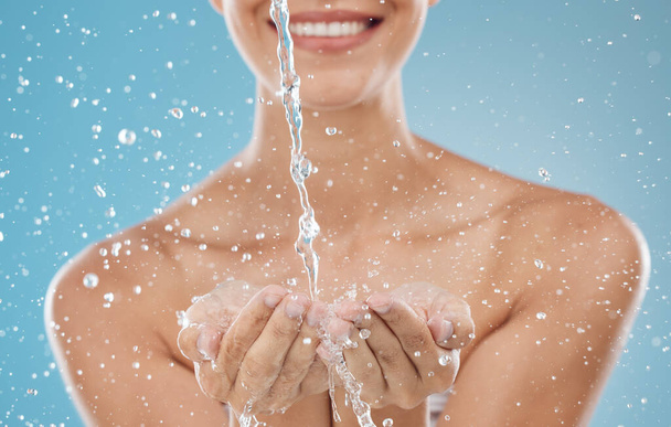 Skincare, water and hands on blue background in studio for hydration, refreshing and facial cleanse. Splash, wellness and woman ready to clean face for washing, moisturizing and hydrate healthy skin. - Photo, image