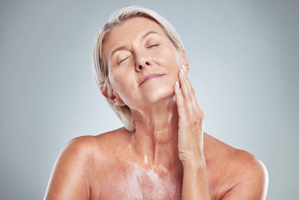 Senior woman, relax and skincare beauty for cosmetics, moisturizer or treatment against a grey studio background. Elderly female hand touching face in satisfaction for perfect skin or facial care. - Фото, зображення