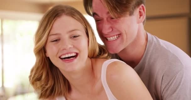 Attractive male hugging happy girlfriend from behind inside room in apartment. Casual portrait of young couple embracing inside home, smiling and laughing. 4k - Footage, Video
