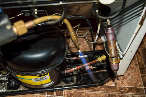 Zuurstofgas lassen tijdens de reparatie van een koelkast. Zuurstof lassen. Koelunit motor. Onderhoud. Reparatie van huishoudelijke apparaten. Industriële apparatuur. - Foto, afbeelding