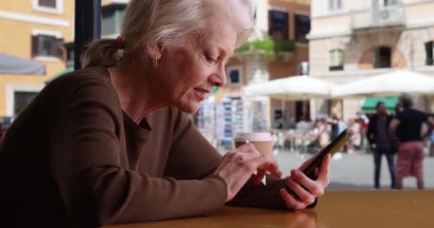 Happy senior touriste réservation vol sur téléphone portable tout en étant assis dans le café de Rome. Femme plus âgée voyageant à travers l'Europe en utilisant un smartphone pour acheter un hôtel et des billets d'avion en Italie. 4k - Séquence, vidéo