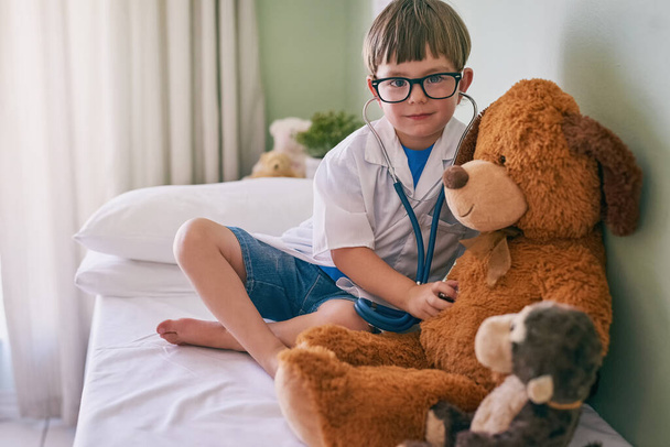 Ez orvosi karriert eredményezhet. egy kisfiú, aki orvosnak adja ki magát, miközben a medvét vizsgálja. - Fotó, kép