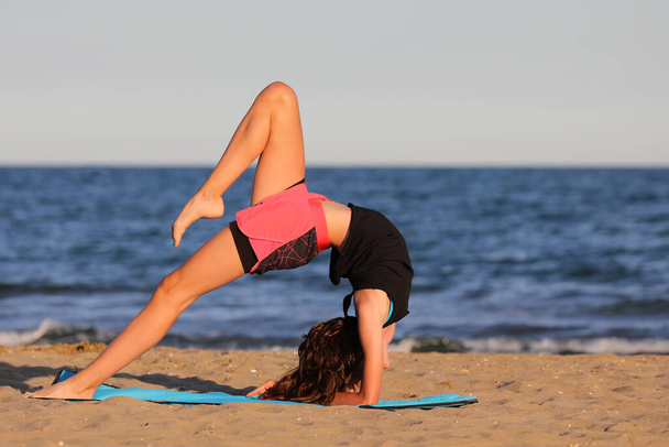 young slender athletic girl does exercises on gym mat on the beach in summer - Foto, immagini