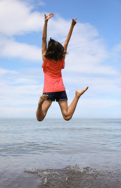 happy girl jumping and rejoicing for joy by the sea in summer - Photo, Image