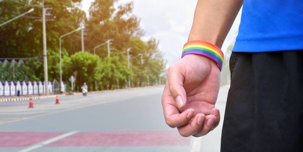 Pulseras de arco iris en manos y muñecas, fondo de calle borroso, concepto para celebraciones de género lgbtq +, confianza en sí mismo de género y llamando a todas las personas a respetar los derechos humanos en el mes del orgullo. - Foto, imagen