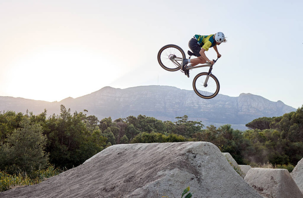 Mountain bike, jump and man doing extreme stunt while training or riding in competition. Bicycle, sports and athlete or cyclist practicing skill for fitness, contest or tournament in nature by a rock. - Foto, immagini