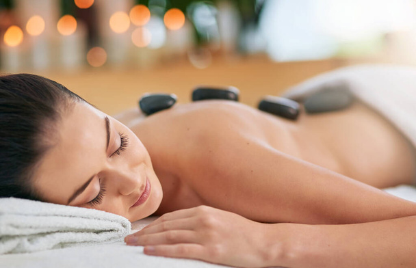 Het is een kans om in rustige tijden te zweven. een aantrekkelijke jonge vrouw genieten van een hete steen massage in een spa - Foto, afbeelding
