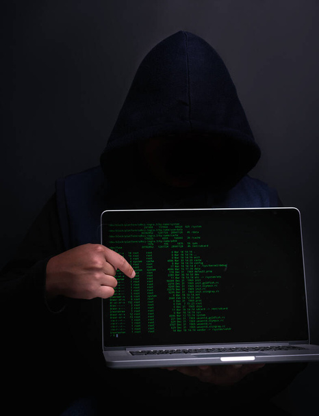 Tu pourrais être la prochaine victime. Portrait d'un hacker méconnaissable tenant un ordinateur portable sur un fond sombre - Photo, image