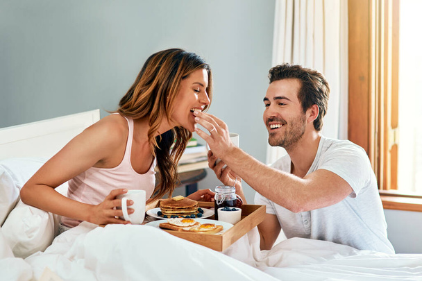 Проснись и пой, а потом вино и ужин. счастливая молодая пара наслаждается завтраком в постели вместе дома - Фото, изображение