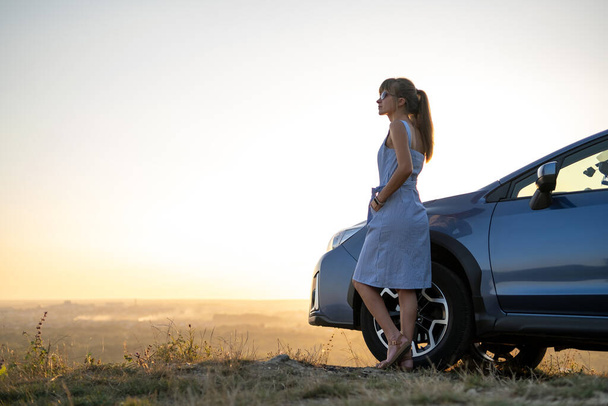 Mladá žena řidič odpočívá v blízkosti svého auta těší teplé letní večer. Koncept cestování a útěku. - Fotografie, Obrázek