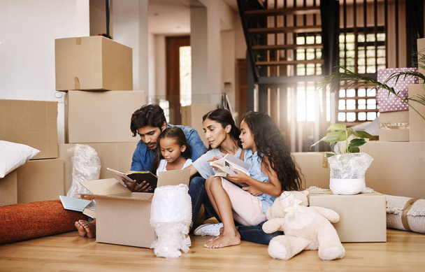 Распаковывать коробку с воспоминаниями. Полный снимок любящей молодой семьи, распаковывающей свои коробки в день переезда - Фото, изображение