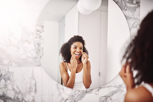 Мы чистим зубы зубной нитью и улыбаемся с этой стороны. привлекательная молодая женщина чистит зубы в ванной комнате дома - Фото, изображение