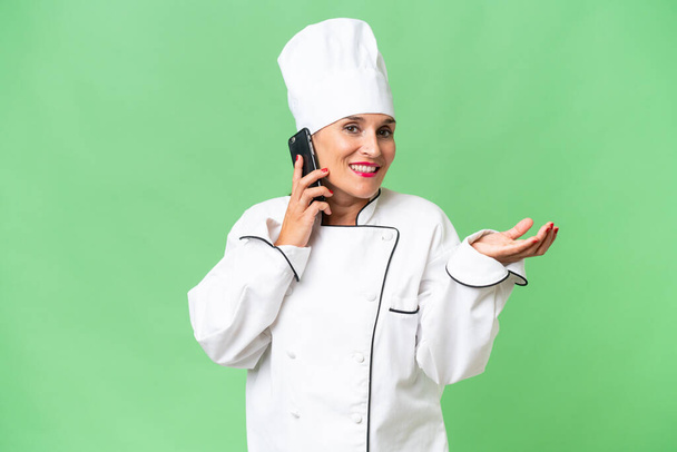 Mujer chef de mediana edad sobre fondo aislado mantener una conversación con el teléfono móvil con alguien - Foto, Imagen
