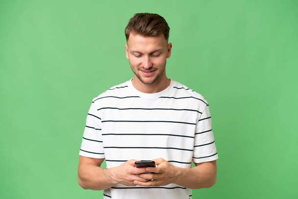 Jeune homme caucasien blonde sur fond isolé envoyer un message avec le mobile - Photo, image