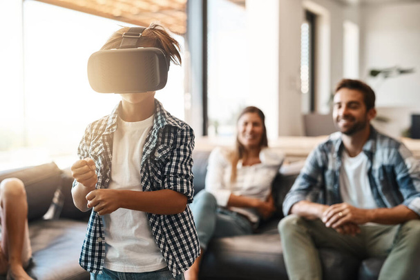 Faire l'expérience de la réalité virtuelle pour la première fois. un petit garçon utilisant un casque de réalité virtuelle à la maison avec ses parents en arrière-plan - Photo, image