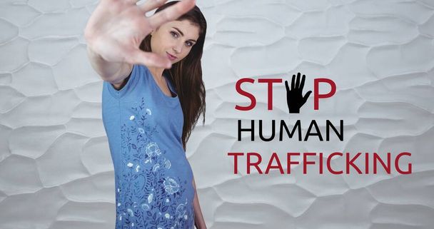 Composite of stop human trafficking text over caucasian woman showing stop sign against wall. Copy space, gesture, crime, freedom, awareness and prevention concept. - Photo, image