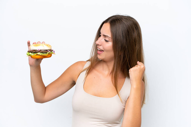 Молода красива жінка тримає бургер ізольовано на білому тлі, відзначаючи перемогу
 - Фото, зображення