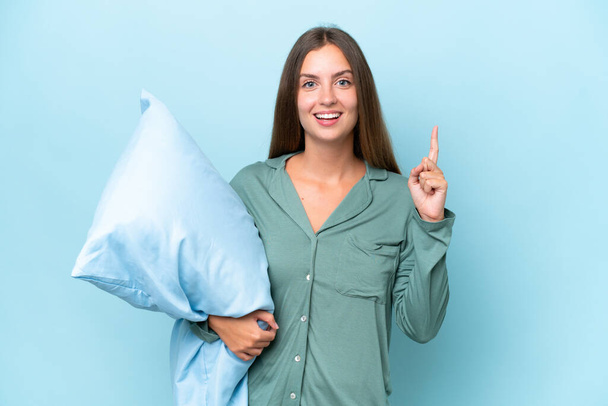 Young beautiful woman isolated on blue background in pajamas and pointing up a great idea - Photo, Image