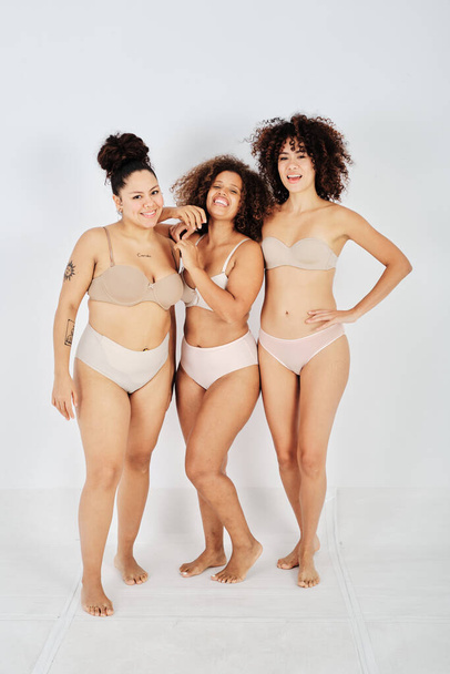 Full body of cheerful multiracial female friends in lingerie with different body standing in studio and looking at camera - Photo, Image