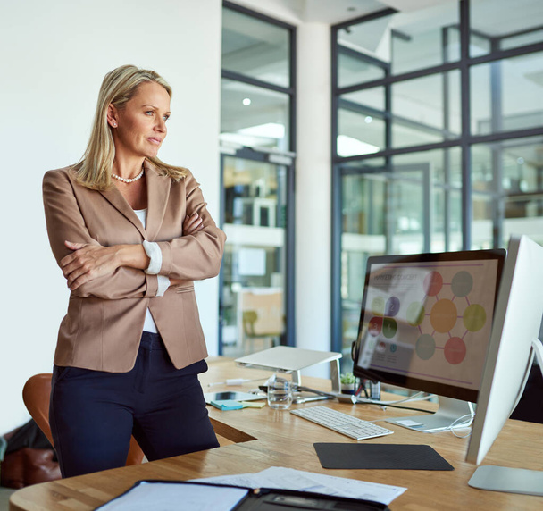 Subiendo a alturas inigualables en su carrera. una mujer de negocios madura mirando reflexivo mientras está de pie en una oficina - Foto, Imagen