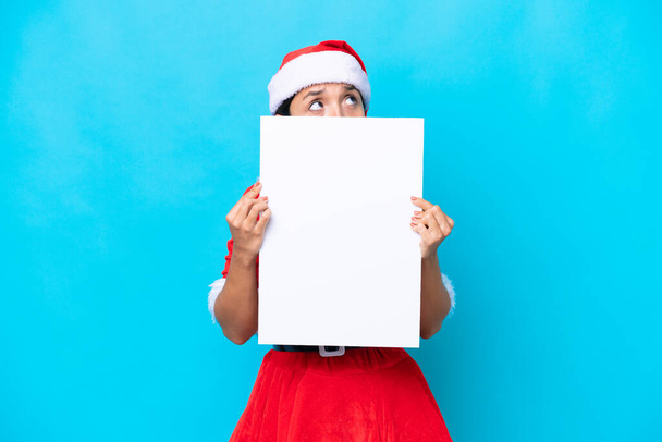 Young hispanic woman dressed as mama noel isolated on white background holding an empty placard and hiding behind it - Photo, Image