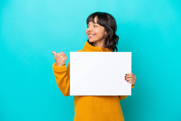 Young latin woman isolated on blue background holding an empty placard and pointing side - Foto, imagen