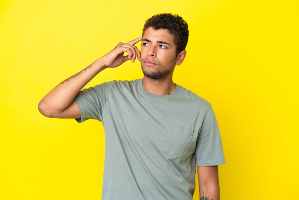 Jonge knappe Braziliaanse man geïsoleerd op gele achtergrond het maken van het gebaar van waanzin zetten vinger op het hoofd - Foto, afbeelding