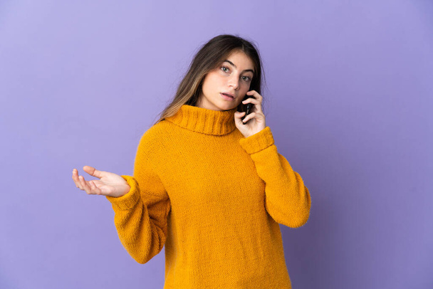 紫色の背景に孤立した若い白人女性誰かと携帯電話との会話を保つ - 写真・画像