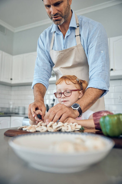 Father, girl in kitchen and cooking food together for healthy, organic family lunch and cutting vegetables at home. Dad teaching child nutrition, learning to cook with smile and fun bonding with love. - Photo, Image