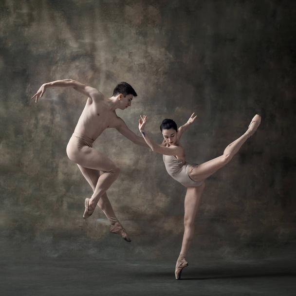 Young man and woman, ballet dancers performing isolated on dark green vintage background. Pastel, nude colored clothes. Contemporary ballet. Concept of classic dance, artist, beauty. Copy space for ad - Photo, Image