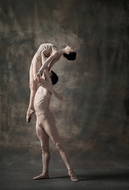 Mladý muž a žena, baletní tanečníci vystupující izolovaně na tmavozeleném vinobraní. Zvedá se. Současný balet. Koncept klasického tance, umělce, krásy. Kopírovat prostor pro inzerci - Fotografie, Obrázek