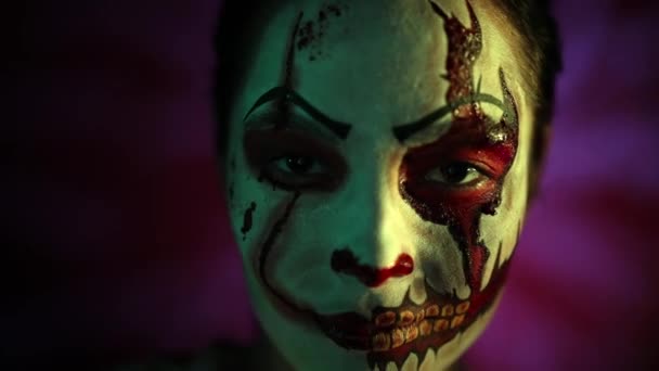 Young woman portrays bloodthirsty zombie with horror teeth and wounds on her face in bloody clothes against dark background with lit. Portrait. Scary image for Halloween. - Footage, Video