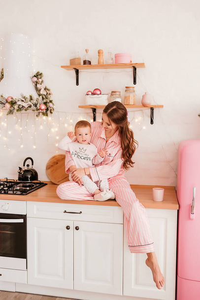 Ano Novo. mãe e filha na cozinha em decorações de Natal em tons rosa claro. Roupas, camisolas quentes. Conceito de ano novo. Foto de alta qualidade - Foto, Imagem