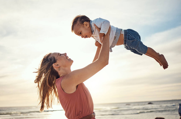 Family, beach and sunset vacation with mother and lifting child in air for fun, love and care with support. Woman and baby happy about bonding experience while on holiday in Bali for summer travel. - Foto, Imagen
