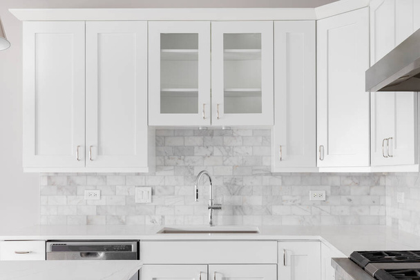 A kitchen sink detail shot with white cabinets and a marble subway tile backsplash. - Fotó, kép