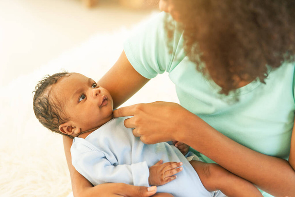 1ヶ月の新生児の息子をベッドルームで丁寧に優しく抱えている若い母親アフリカ系アメリカ人。母親の暖かい抱擁で愛らしい小さな幼児の睡眠も。幸せな母の日のコンセプト - 写真・画像