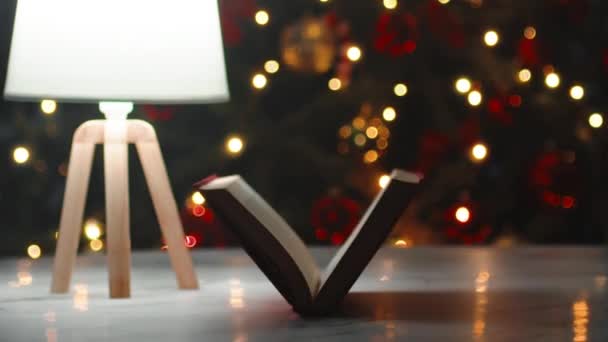 Książka przeglądać na stole z oświetlonym tle choinki - Materiał filmowy, wideo